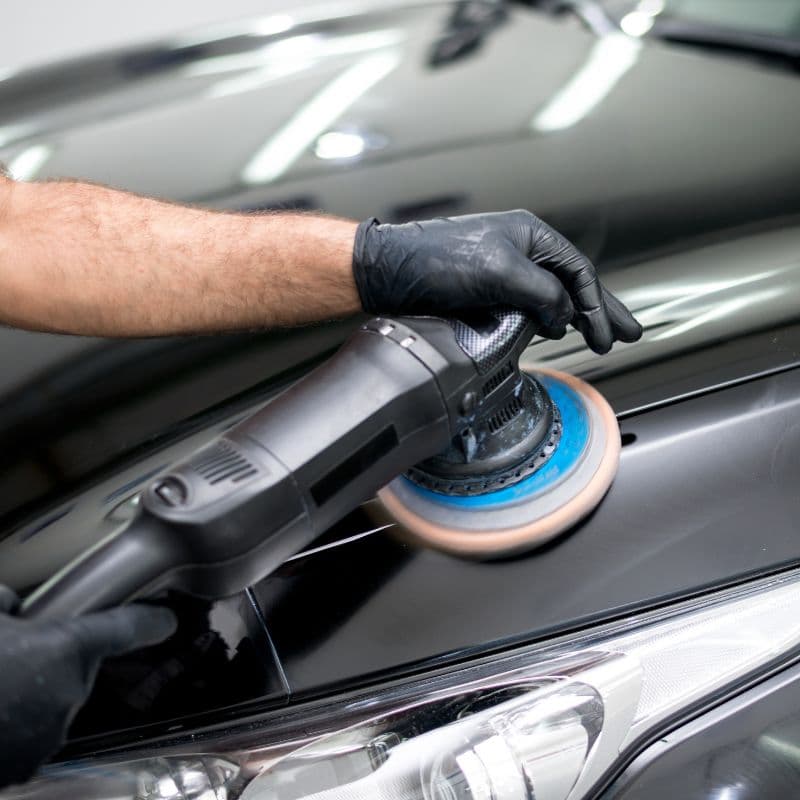 Professional dual-action polisher on a glossy black fleet vehicle hood, precision tool work at scale.