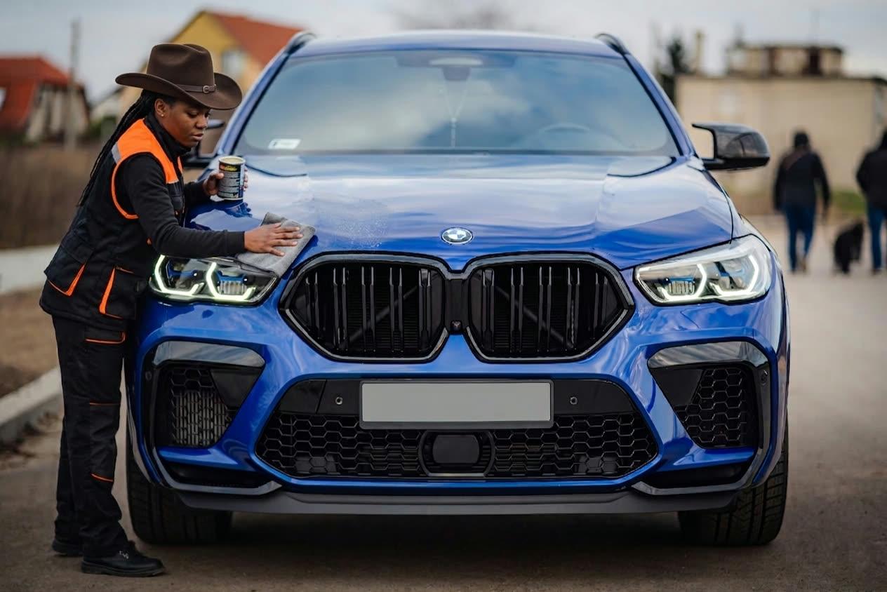 Foam Ranger detailer in a black and hi-vis orange jacket with cowboy hat doing a final wipe-down on a deep blue BMW X6.