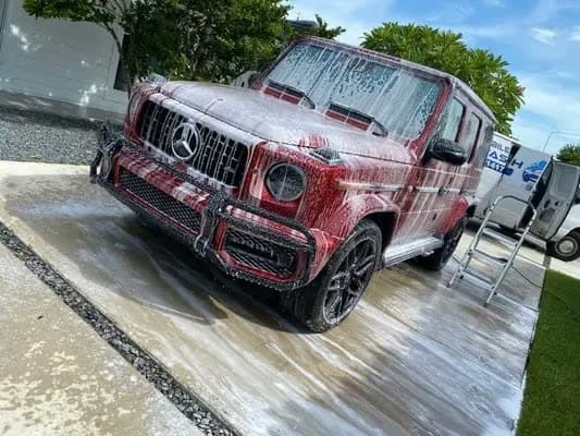 Red Mercedes G-Class covered in thick white foam during a foam-cannon pre-wash.