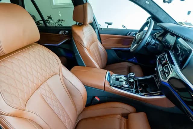 Post-detail closeup of tan quilted leather seats in a luxury SUV, ambient blue accent lighting.